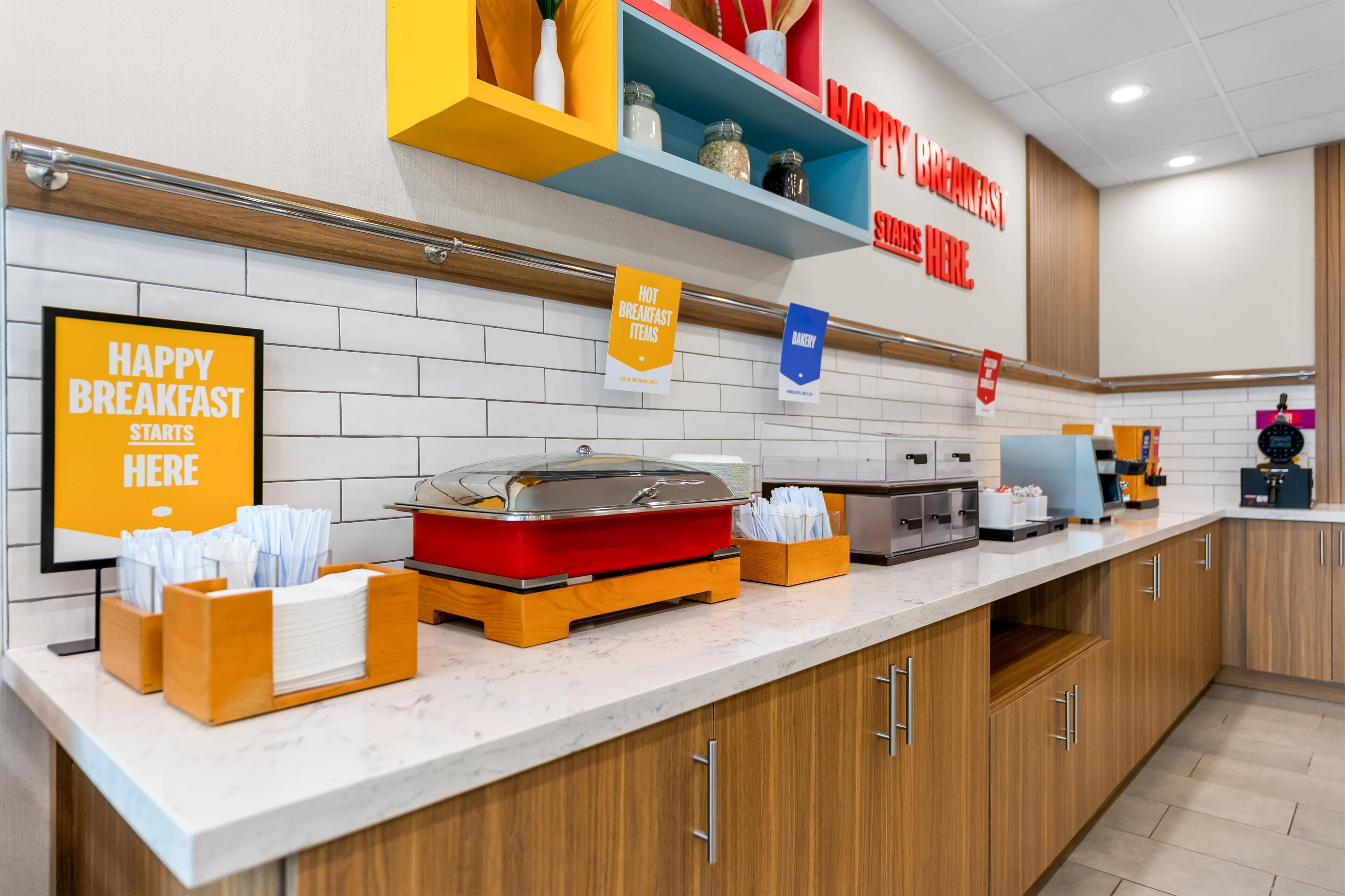 A breakfast buffet setup with a sign indicating 'HAPPY BREAKFAST STARTS HERE' and a sign for 'HOT BREAKFAST ITEMS'.