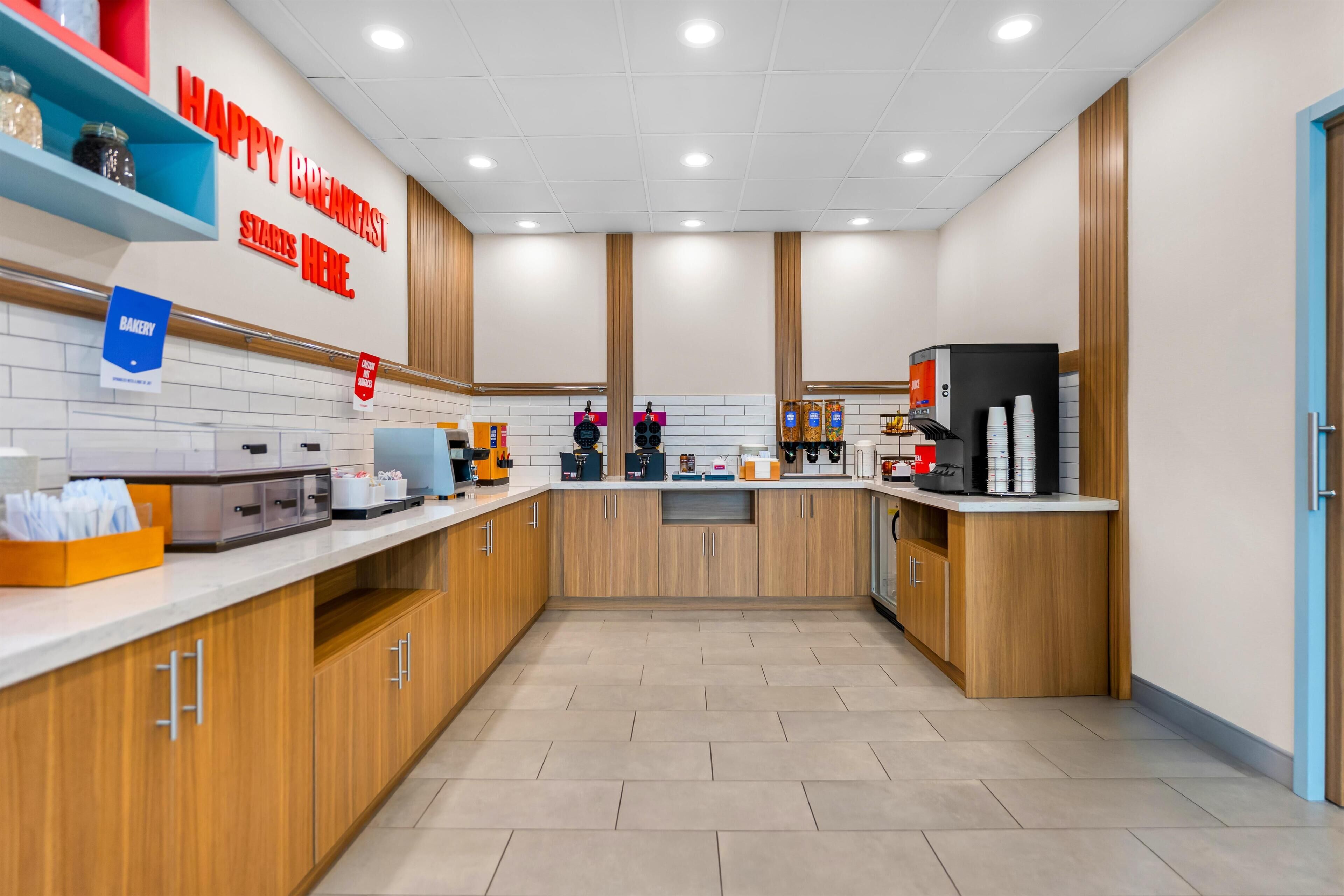 A modern kitchen with a 'Happy Breakfast Starts Here' sign, a bakery section, and a coffee station.