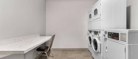 A laundry room with a marble countertop, a chair, and stacked washing machines.