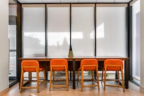 A dining area with a wooden table and four orange chairs, large windows, and a vase on the table.