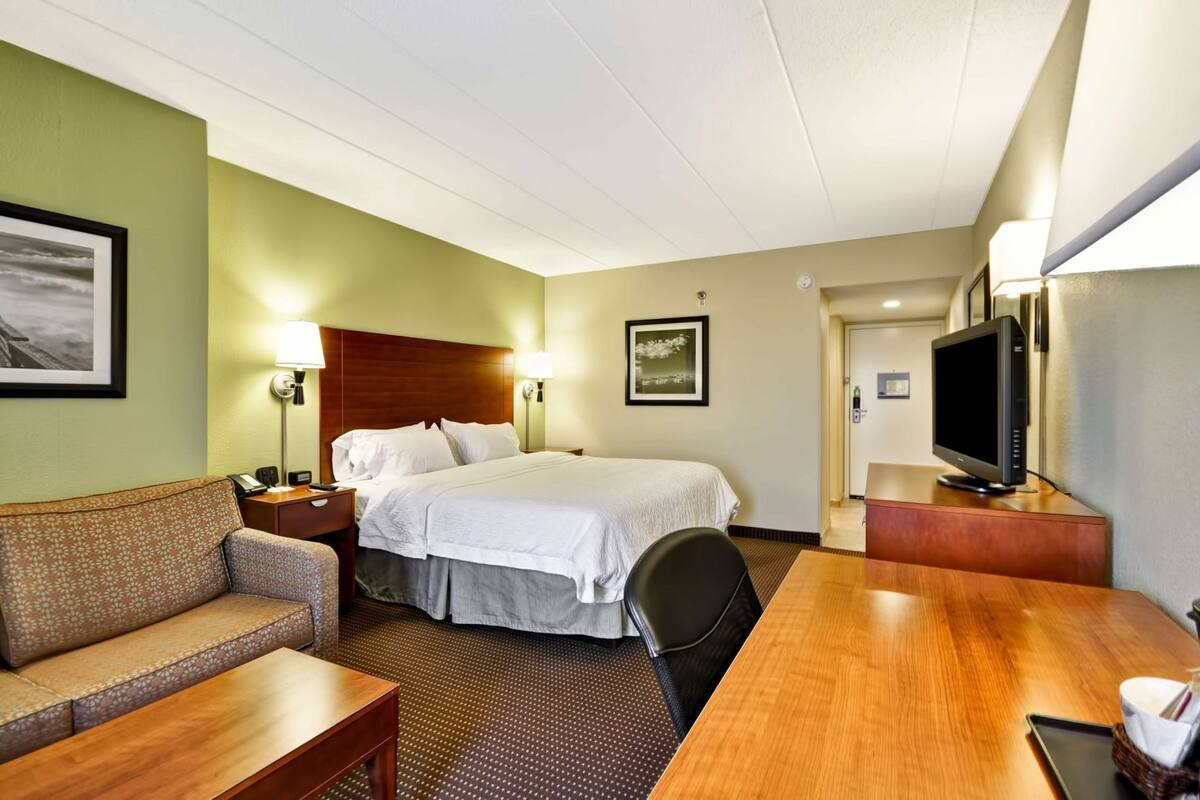 Ett hotellrum med en säng, ett skrivbord, en stol, en tv och en soffa.