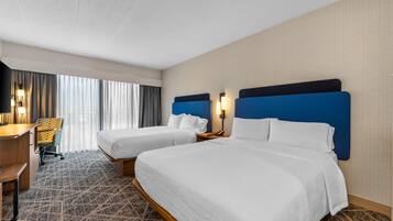 Una habitación de hotel con dos camas, un escritorio, una silla y un ventanal con cortinas.