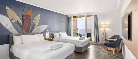 A hotel room with two beds, a desk, a chair, a TV, and a large window with a view.