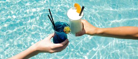 Two hands holding drinks over a pool.