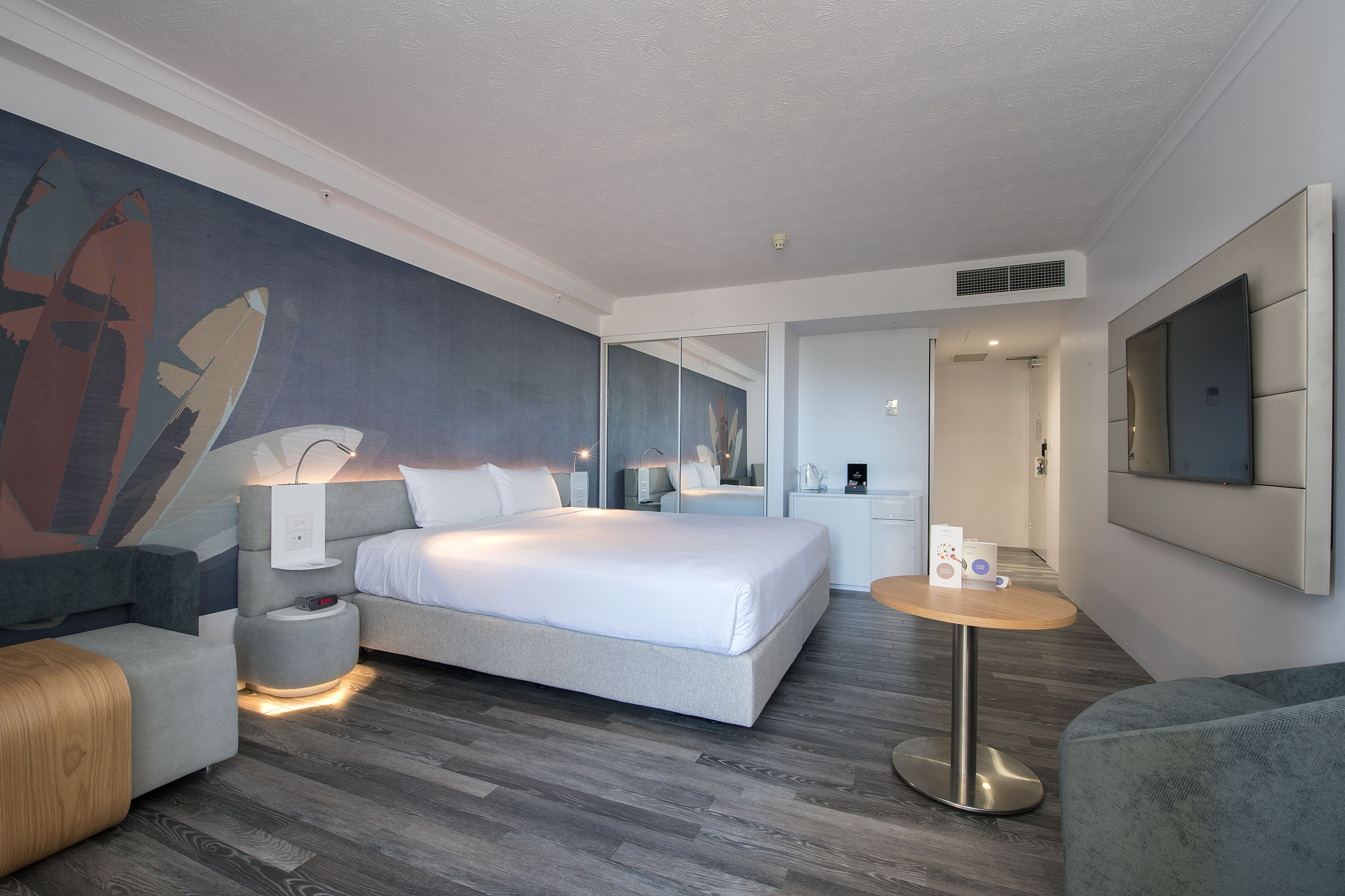 A modern hotel room with a large bed, a seating area, a small table, and a wall-mounted TV.
