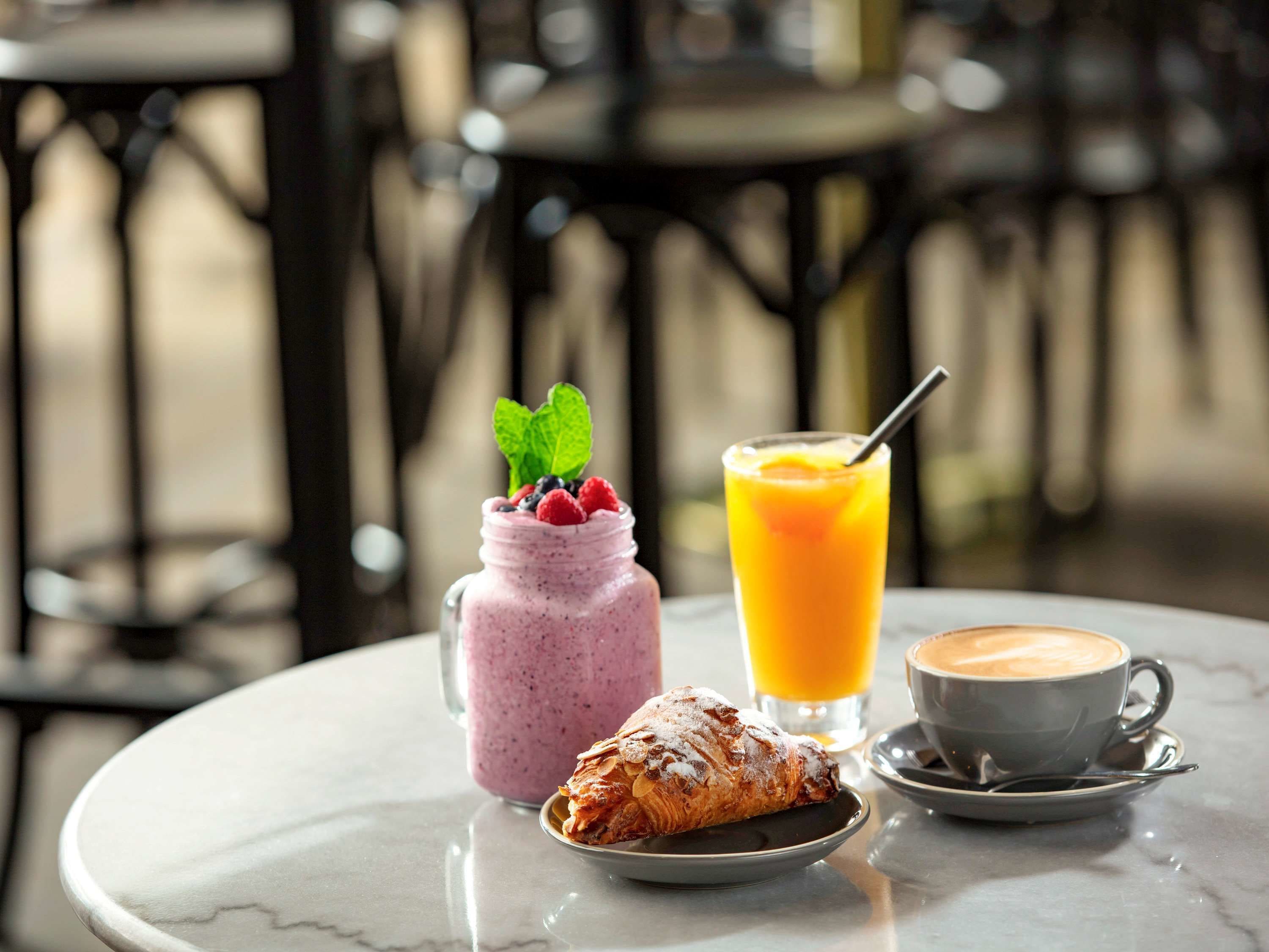 Et bord med dessert, en smoothie, et glas appelsinjuice og en kop kaffe.