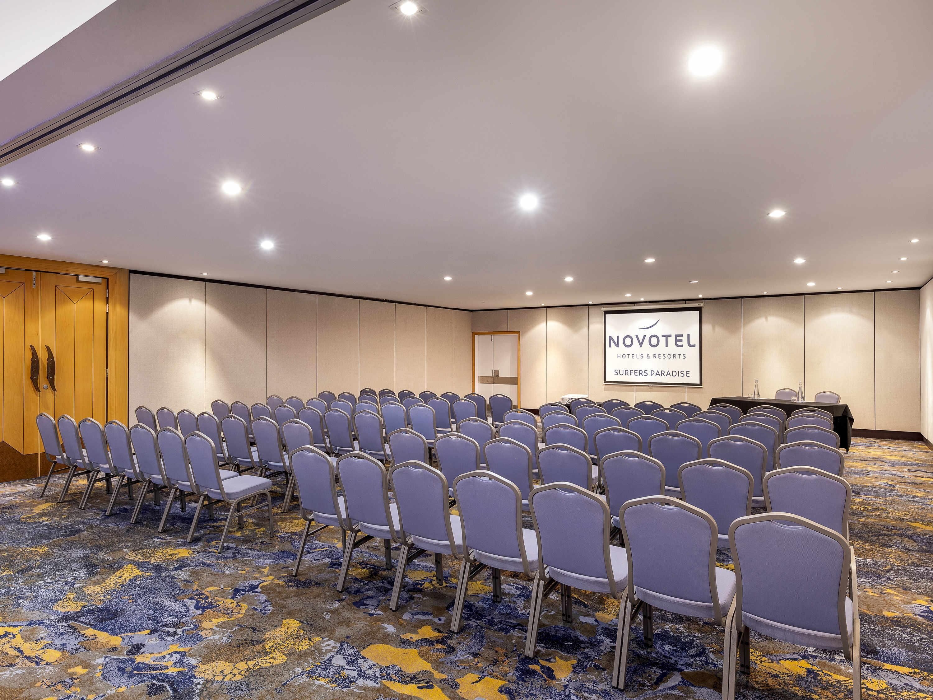 A conference room with rows of chairs, a projection screen, and a carpeted floor.