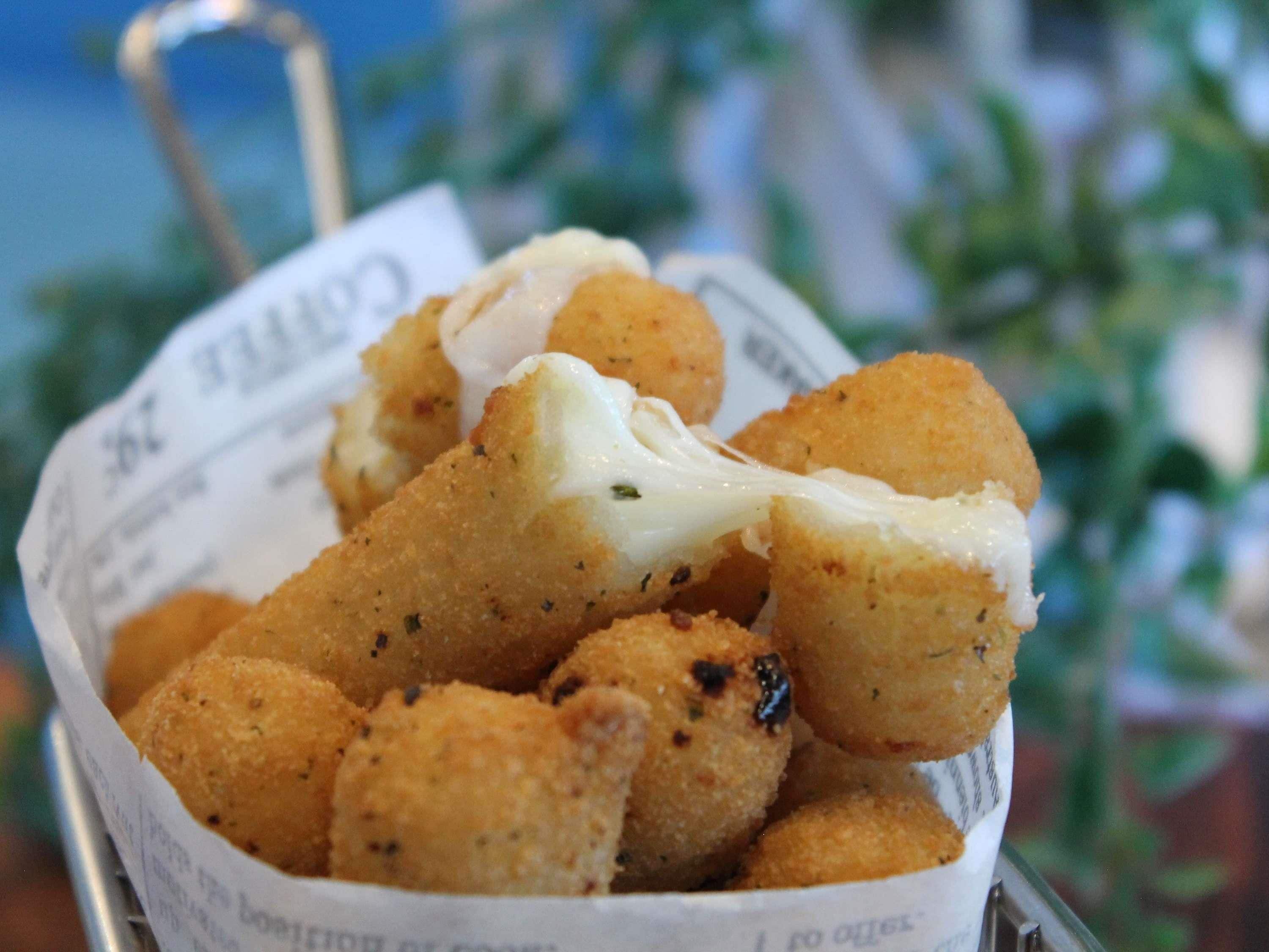 A basket of breaded and fried food items, possibly cheese sticks, with a creamy sauce.