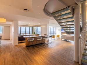 Ein modernes Interieur mit einer zentralen Bar, einer Sitzgelegenheit und einer Wendeltreppe.