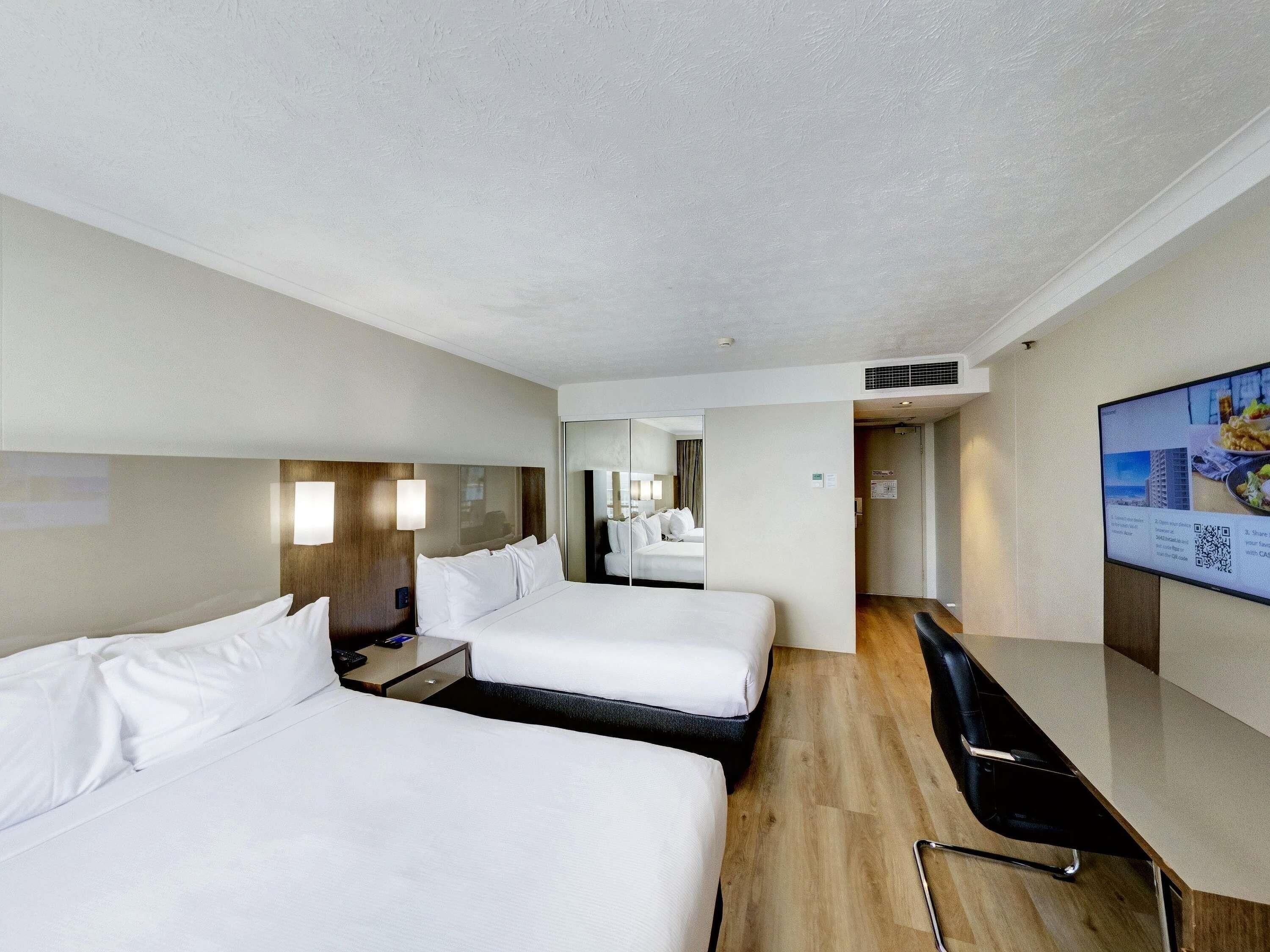A hotel room with two beds, a desk, a chair, a TV, and a mirror.