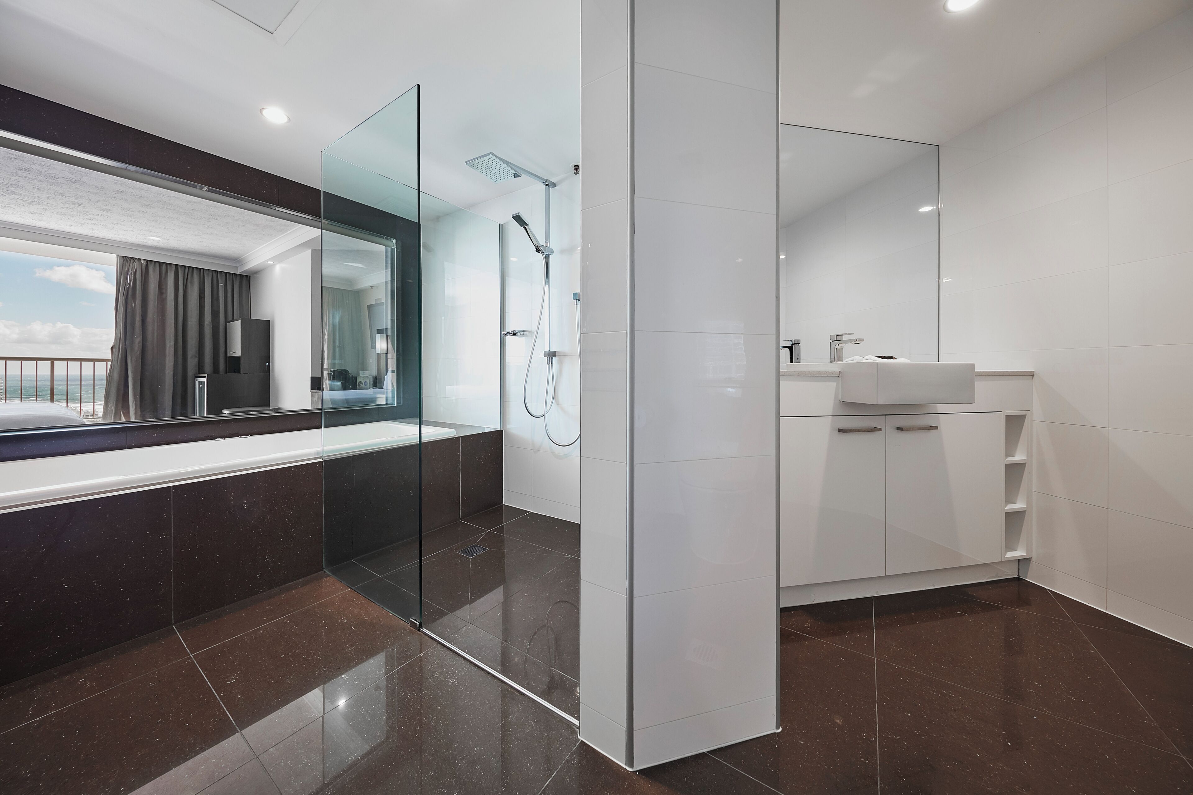 A modern bathroom with a glass shower enclosure, a large mirror, and a view of the city.