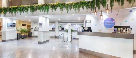 A modern hotel reception area with a clean, polished floor, a reception desk, and a wall adorned with hanging plants.