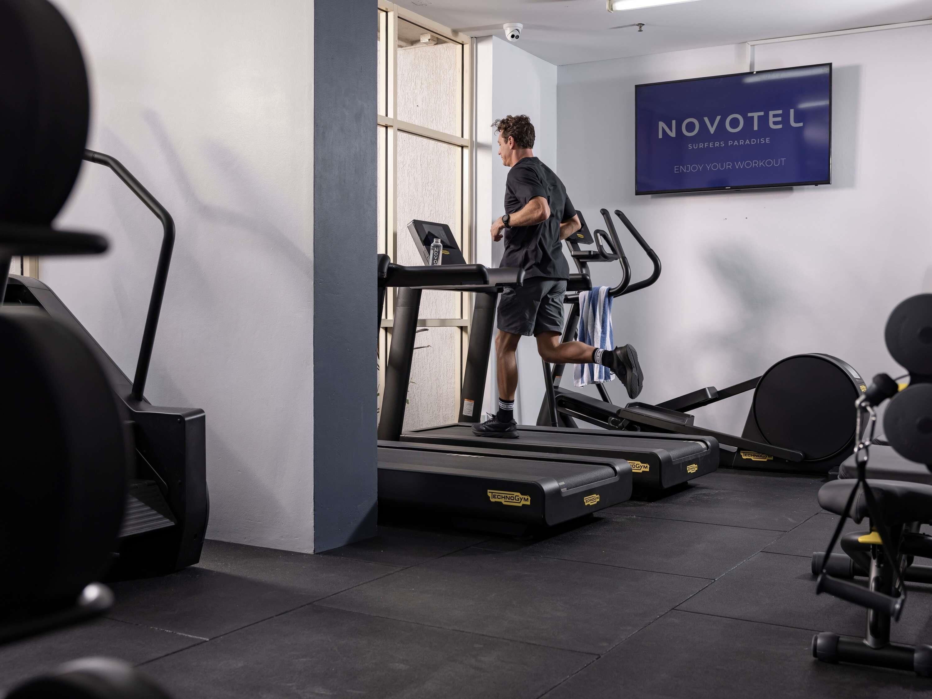 A gym with treadmills, a wall-mounted sign reading 'NOVOTEL,' and a door leading outside.