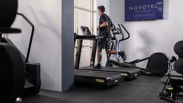 A gym with treadmills, a wall-mounted sign reading 'NOVOTEL,' and a door leading outside.