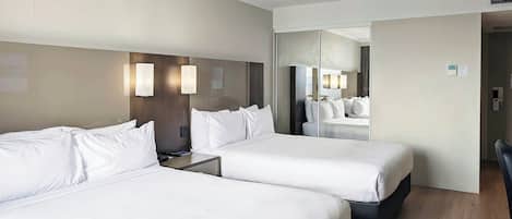 A hotel room with two beds, a large mirror, and a wooden floor.