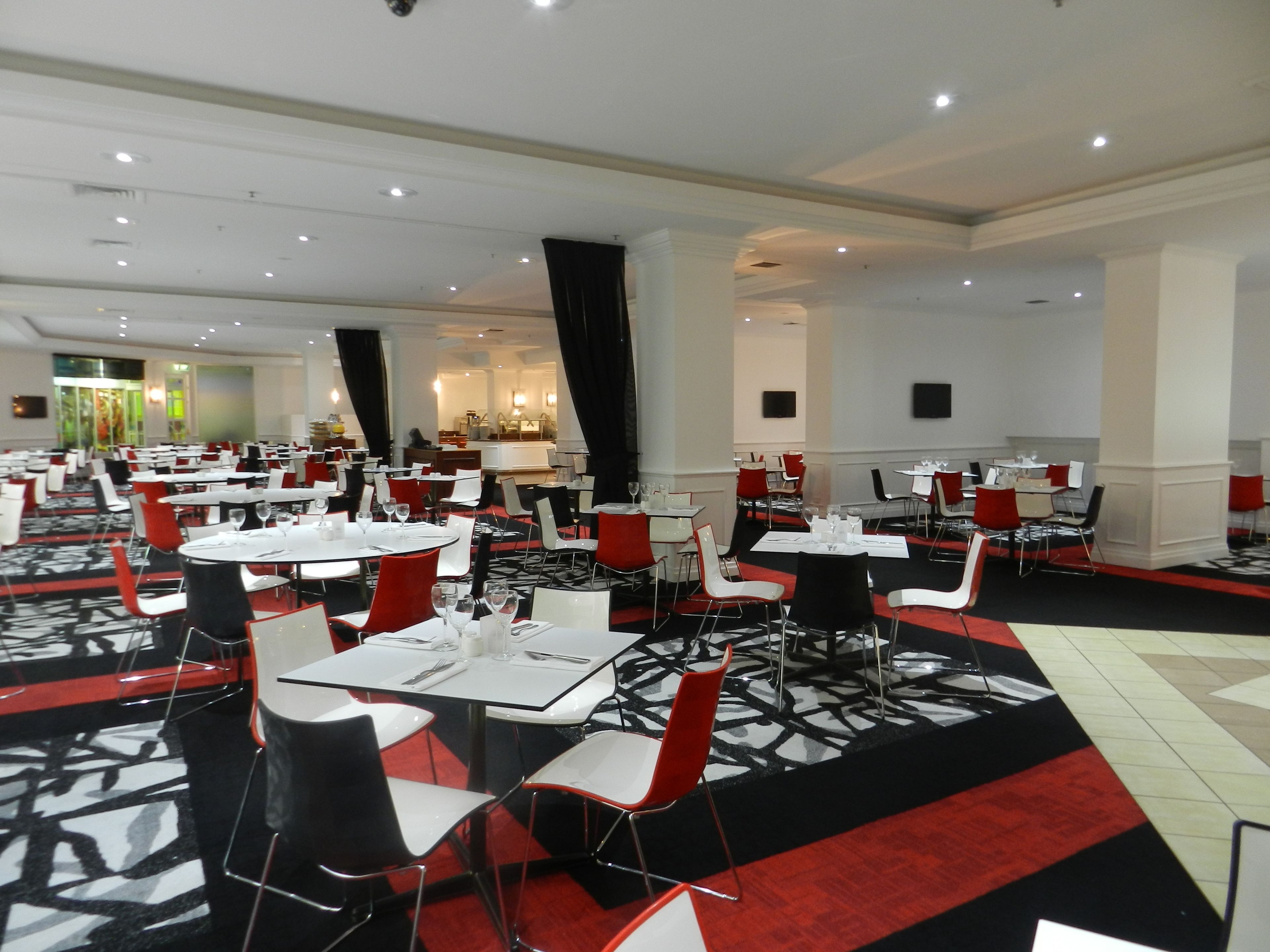 Un vaste espace dédié à la salle à manger, avec plusieurs tables et chaises, une moquette à motifs et un aménagement intérieur moderne.