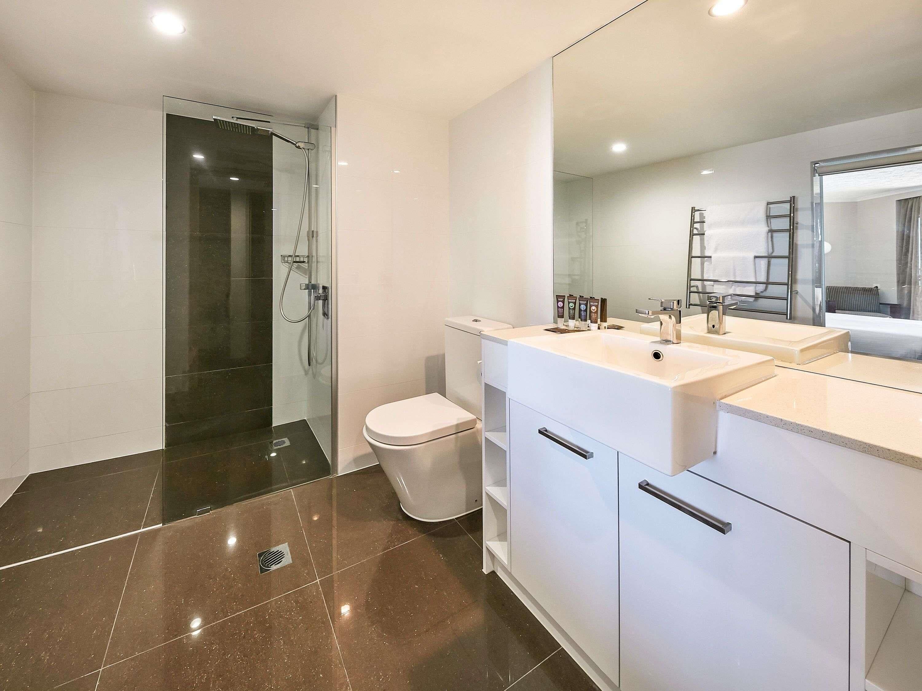 A modern bathroom with a glass shower enclosure, a white toilet, and a vanity with a large mirror.