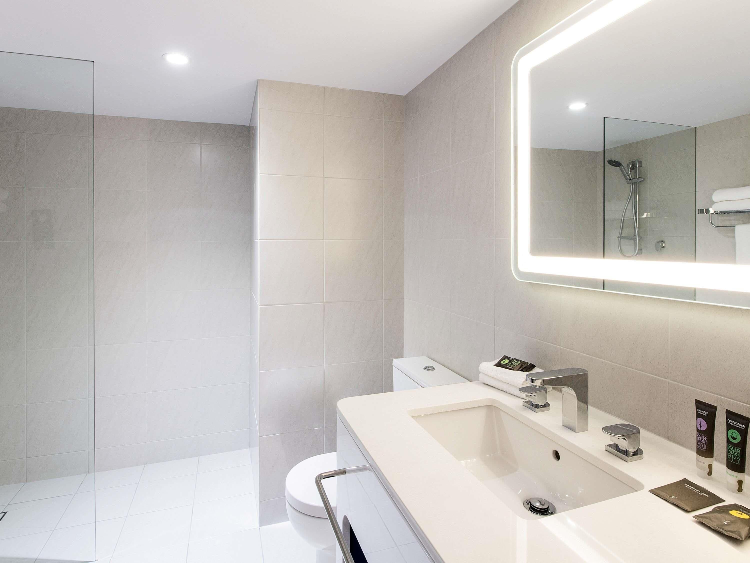 A modern bathroom with a large mirror, a shower, and a toilet.