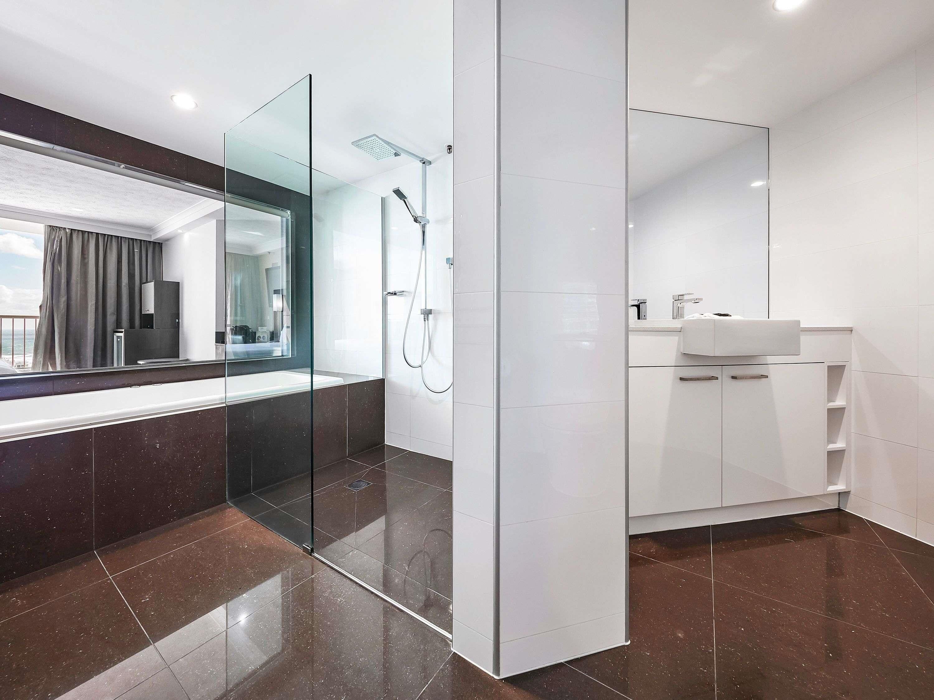 A modern bathroom with a glass partition, a shower, a sink, and a large mirror.