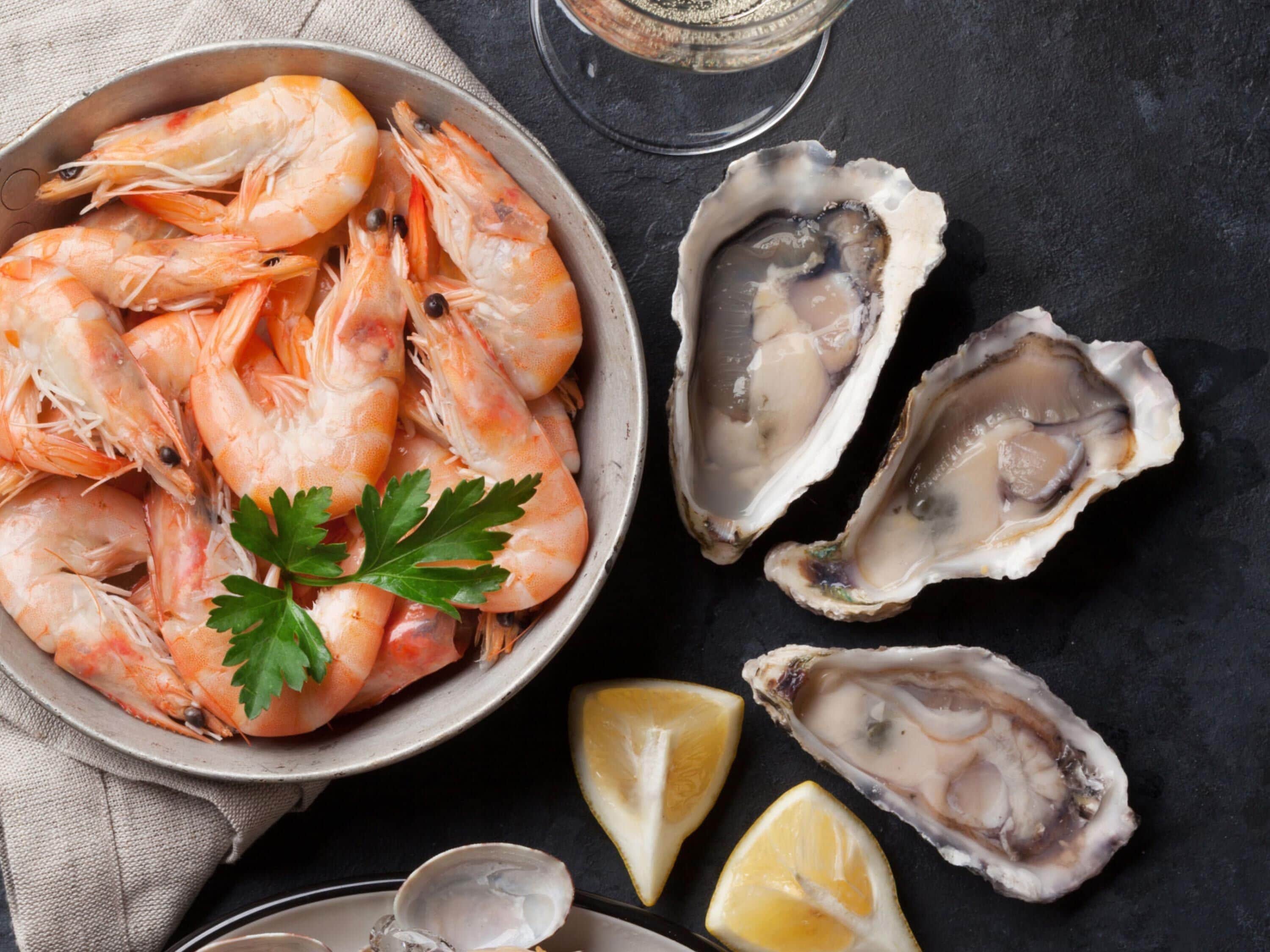 A bowl of cooked shrimp and open oysters on a dark surface.