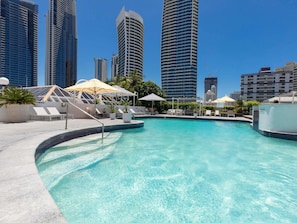A swimming pool with lounge chairs and umbrellas, surrounded by high-rise buildings.