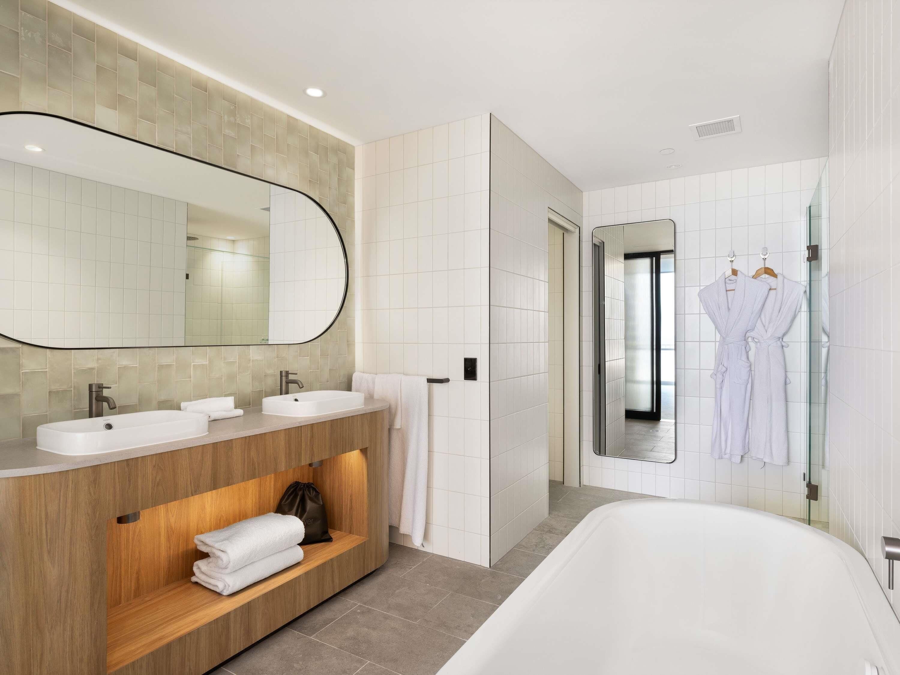 Un baño moderno con un espejo grande, dos lavabos, un tocador con espacio de almacenamiento, una bañera y una zona de ducha.