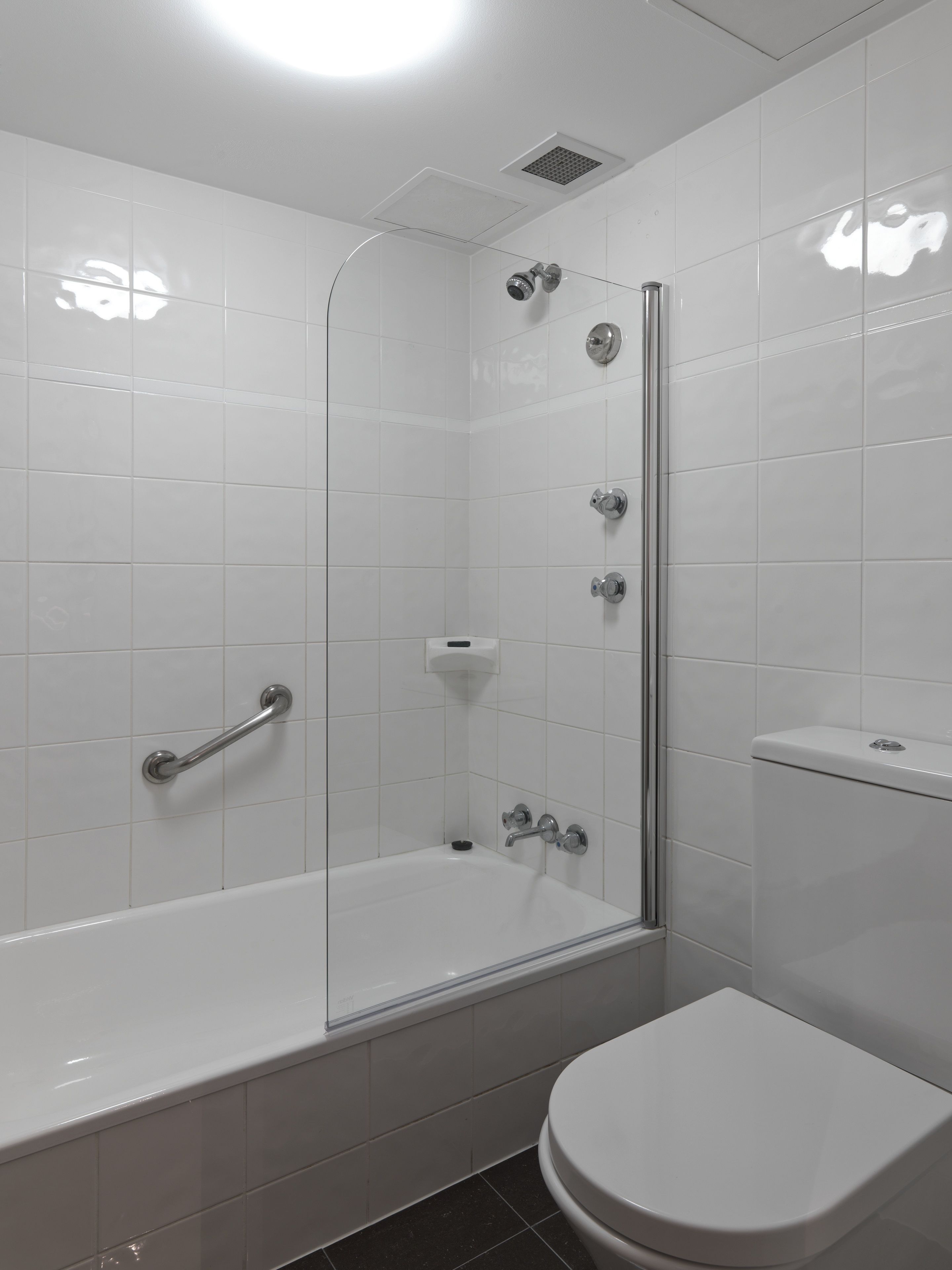 A modern bathroom with a glass-enclosed shower, a white bathtub, and a toilet.