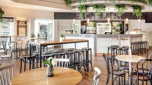A modern cafe with round tables and black chairs, a central bar area, and hanging plants. - Novotel Surfers Paradise (Surfers Paradise)