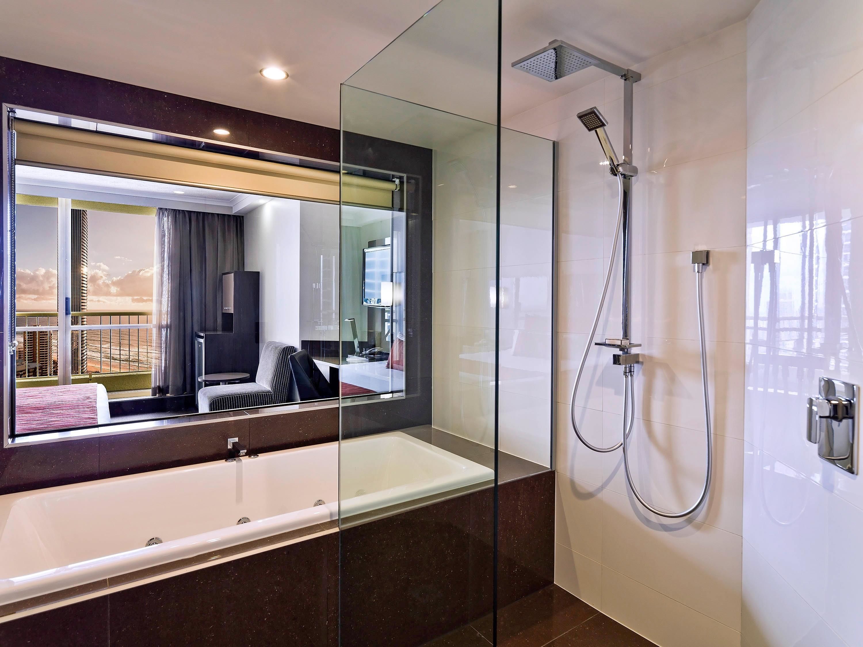 A modern bathroom with a glass-enclosed shower, a large mirror, and a bathtub.