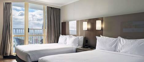 Een hotelkamer met twee bedden, een groot raam met gordijnen, een balkon en uitzicht op de stad.
