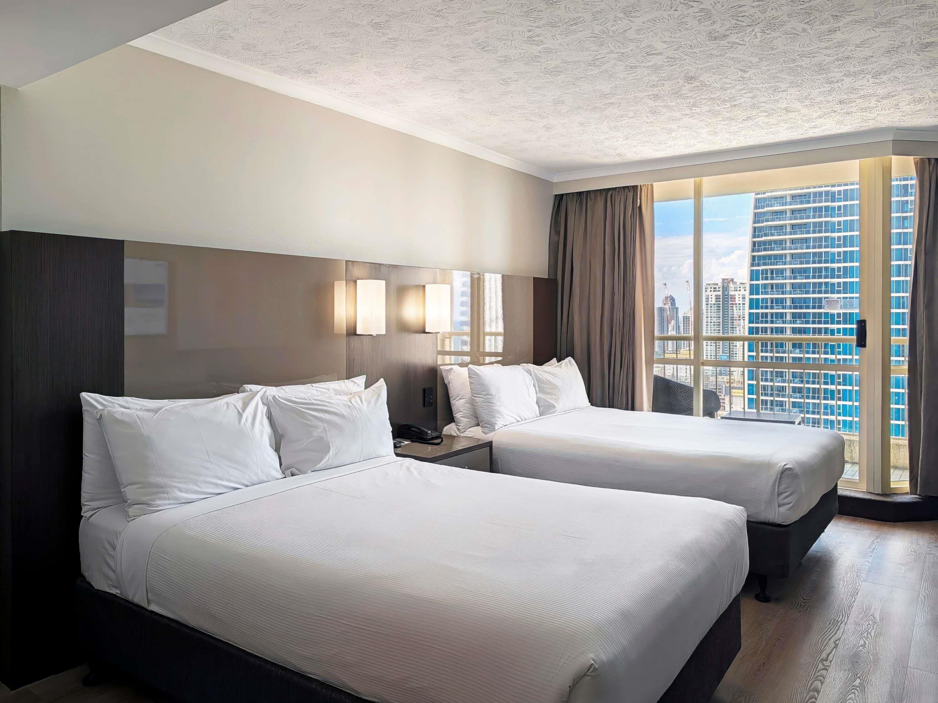 Habitación de hotel con dos camas, vistas a la ciudad y diseño moderno.