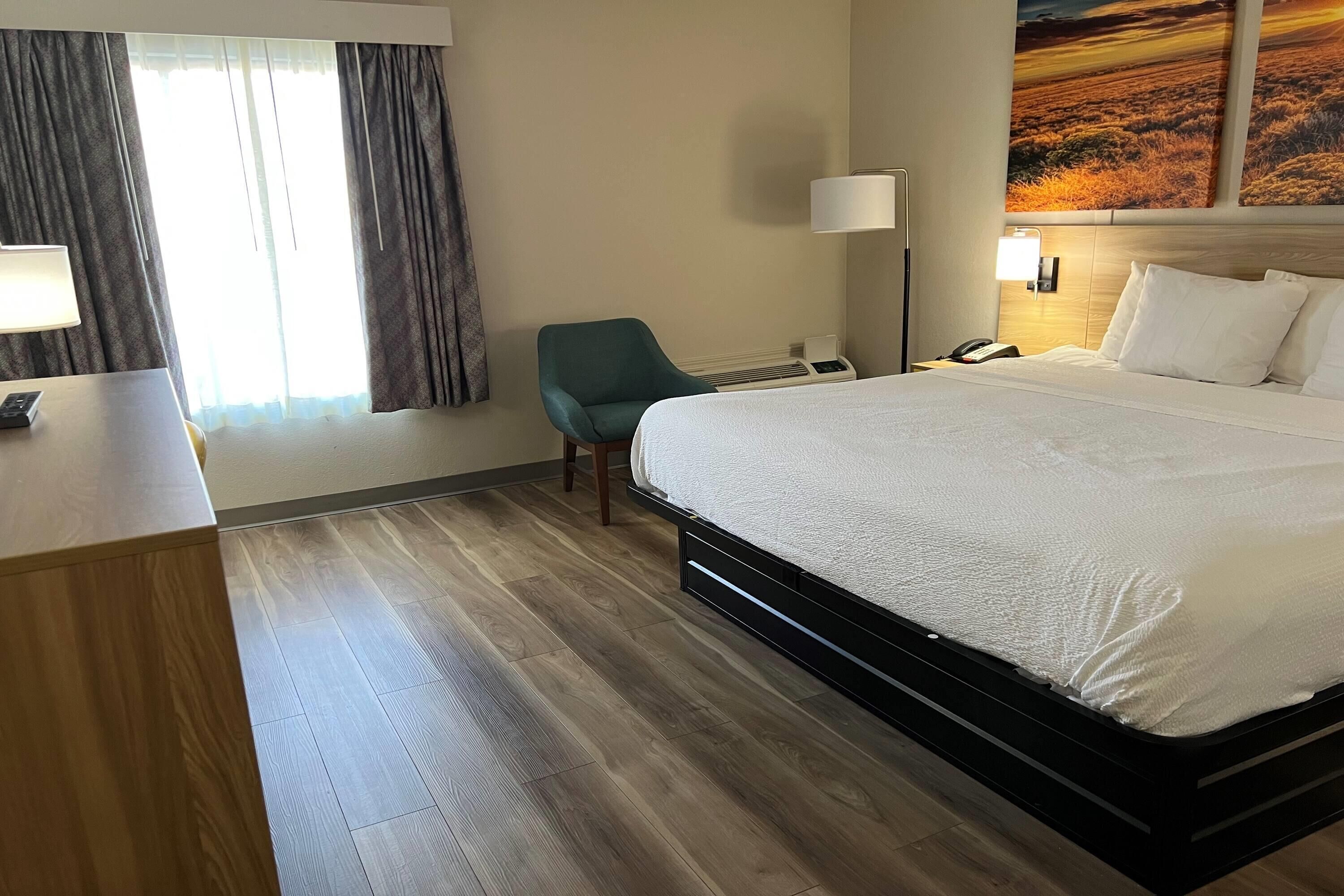 A hotel room with a large bed, a desk with a lamp, a chair, and a painting on the wall.