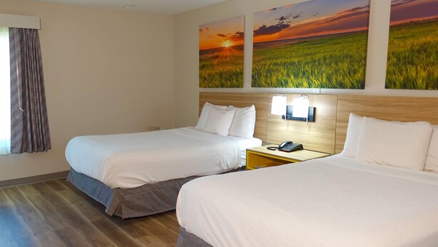 A hotel room with two beds, a wooden headboard, a nightstand with a lamp, and two wall-mounted paintings of fields. - Days Inn by Wyndham Norman (Norman)