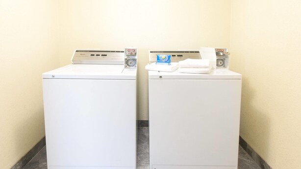 Deux machines à laver à chargement frontal, de couleur blanche, sont placées dans un coin, sur un sol carrelé.