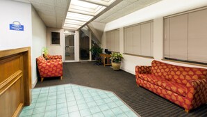 A hotel lobby with a check-in desk, two red patterned sofas, a reception area, and a tiled floor. - Days Inn by Wyndham Norman (Norman)