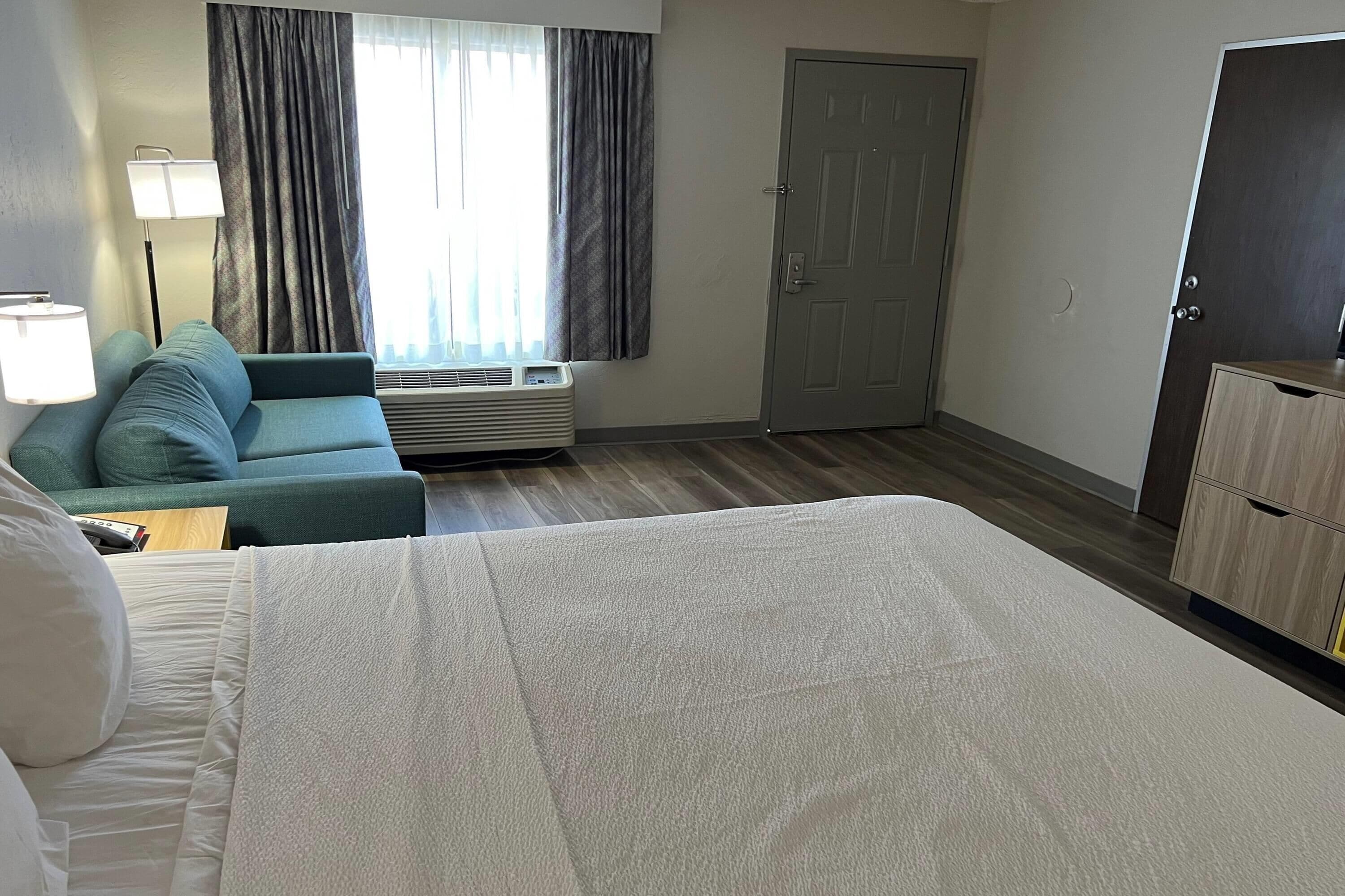 Une chambre d’hôtel comprenant un lit, un canapé, un bureau, une lampe, une fenêtre avec des rideaux, un climatiseur et une armoire.