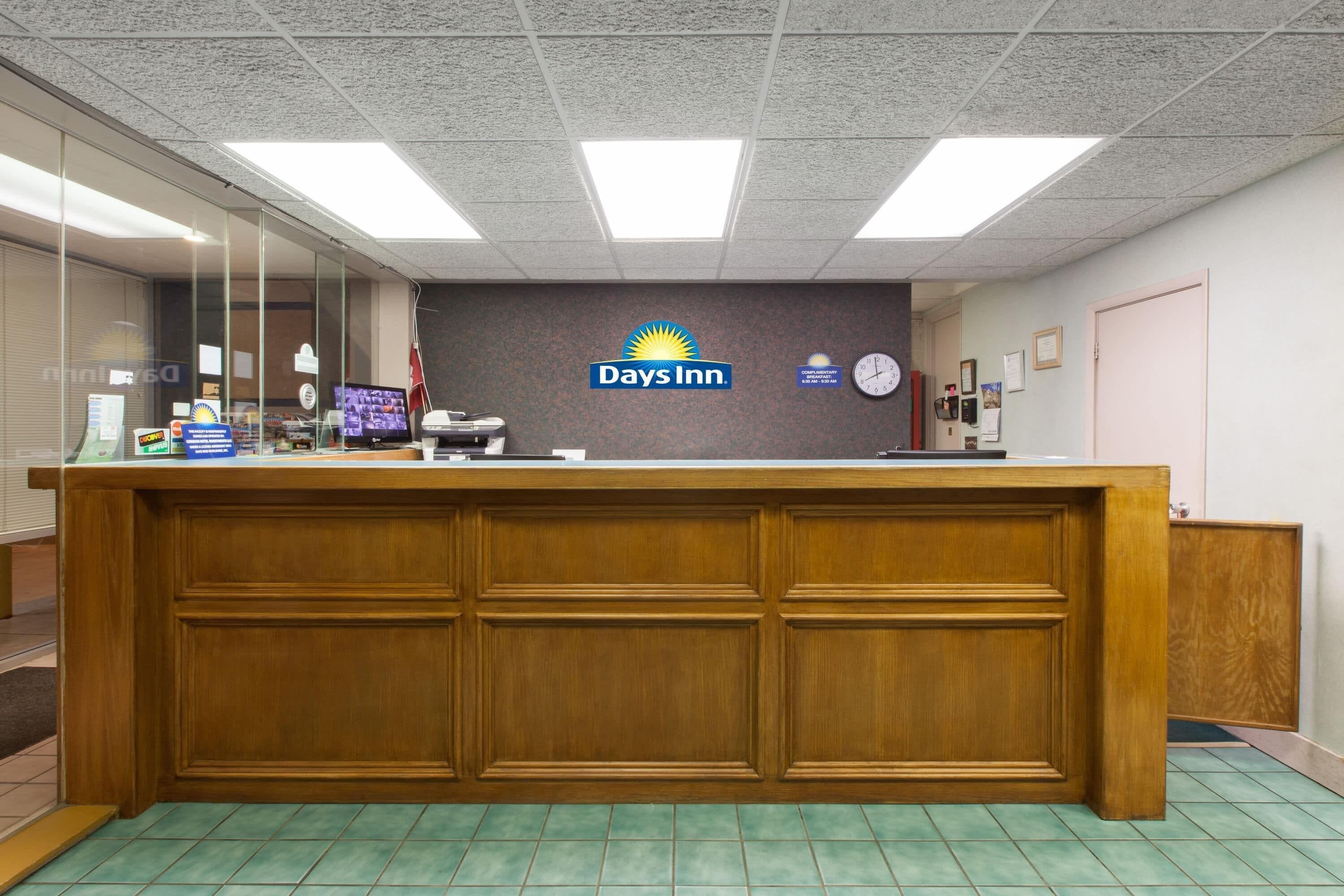 A reception desk with a Days Inn logo, a clock, and a bulletin board.