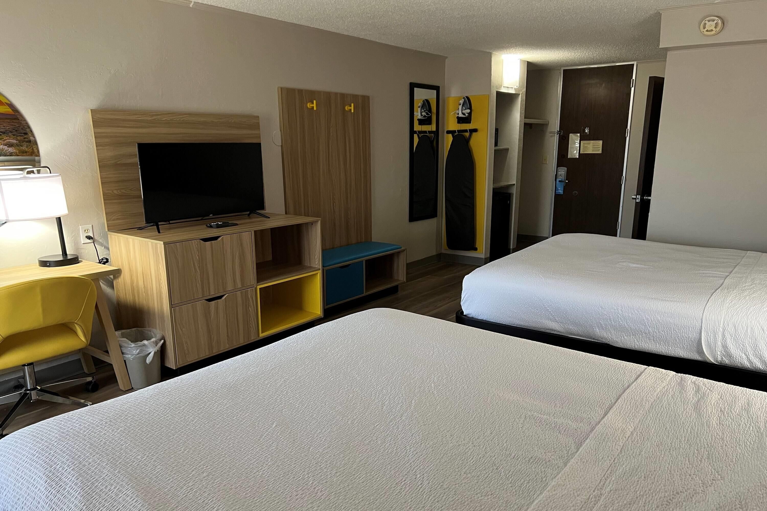 Habitación de hotel con dos camas, televisión, escritorio con lámpara, armario y espejo.