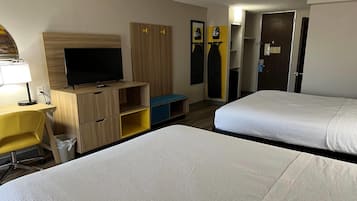 Habitación de hotel con dos camas, televisión, escritorio con lámpara, armario y espejo.