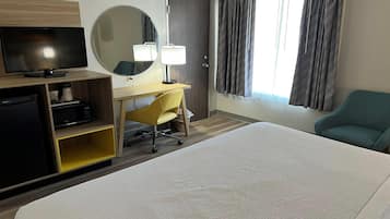 Habitación de hotel con cama, escritorio con silla, televisor, espejo y ventana con cortinas.