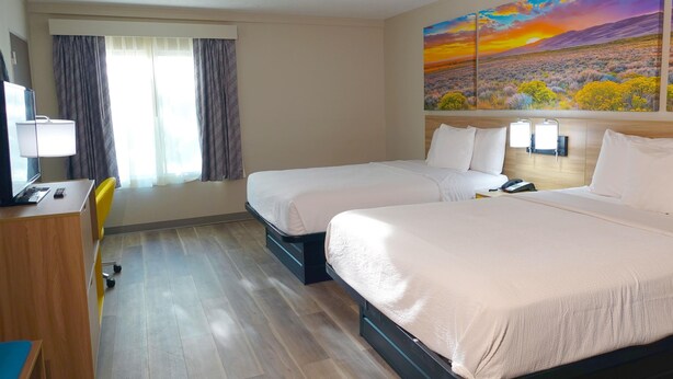 A hotel room with two beds, a desk, a chair, and a large painting on the wall. - Days Inn by Wyndham Norman (Norman)