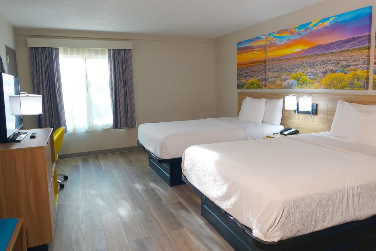 Une chambre d’hôtel avec deux lits, un bureau, une chaise et un grand tableau au mur.