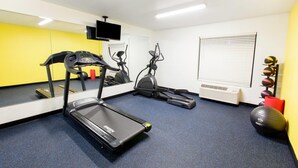 A gym with a treadmill, elliptical, and stationary bike, a mirror, a TV, and exercise balls against a yellow wall. - Days Inn by Wyndham Norman (Norman)