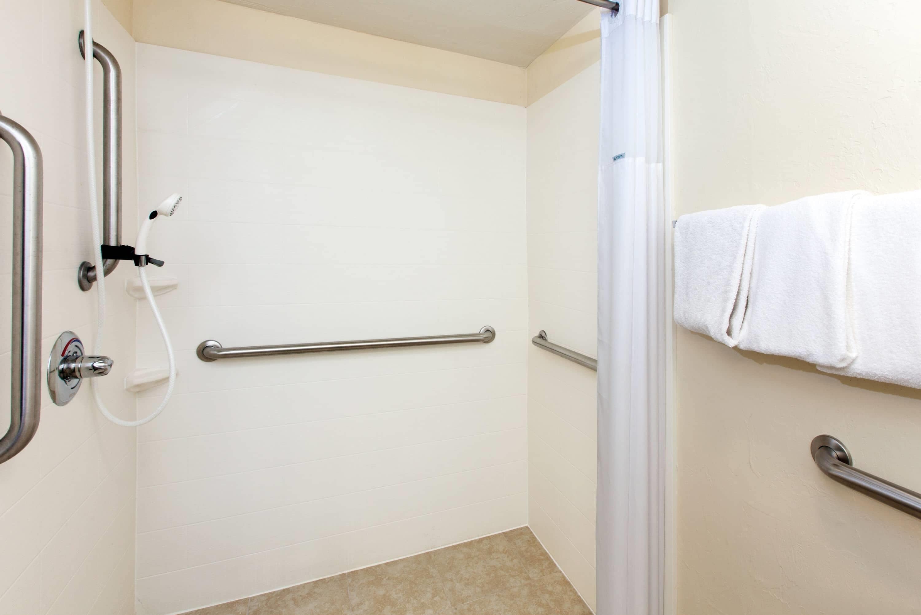 Un baño con paredes de azulejos blancos, zona de ducha y un perchero para toallas.