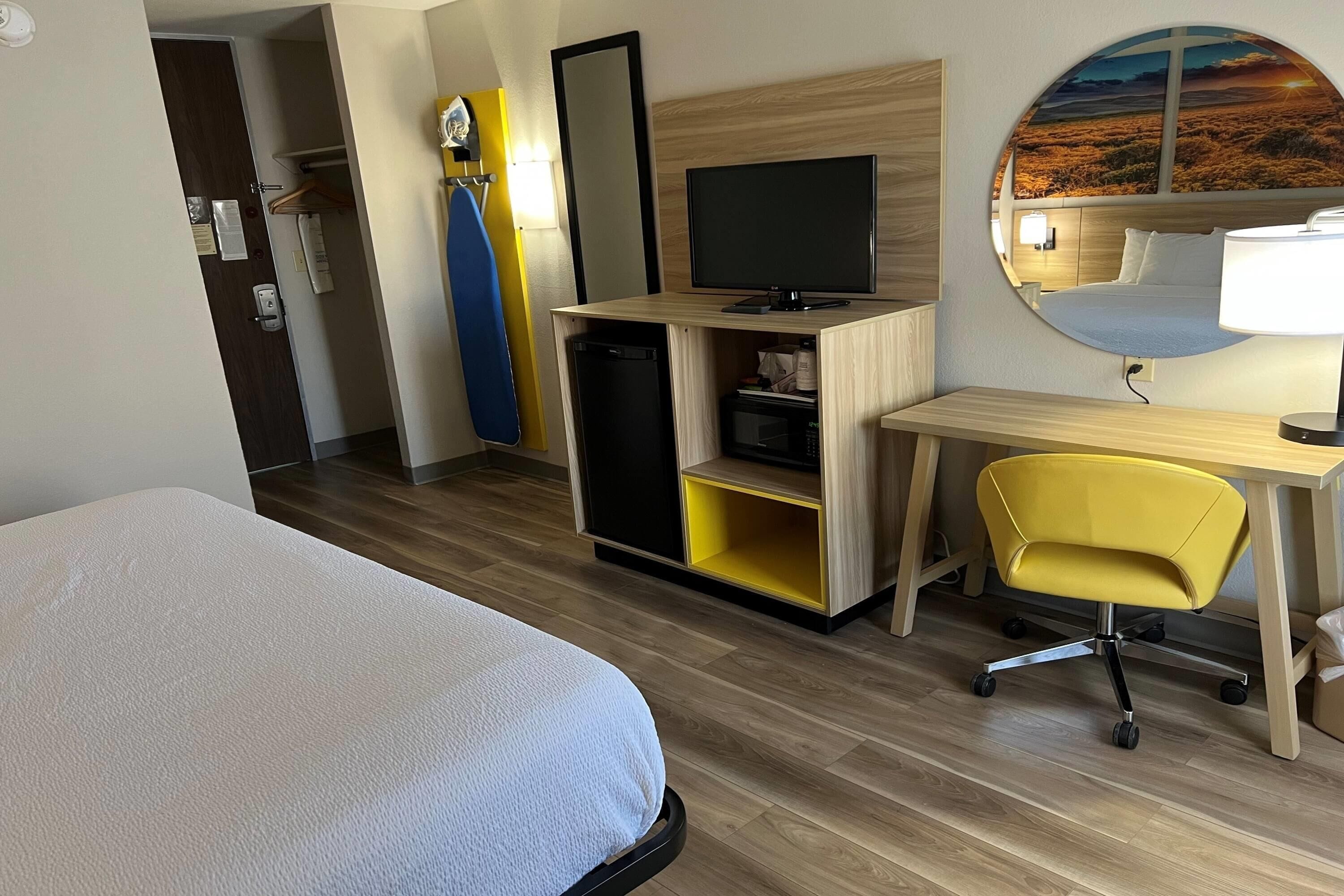 Ein Hotelzimmer mit einem Bett, einem Schreibtisch mit Computer, einem Sessel, einem Fernseher und einem Spiegel.