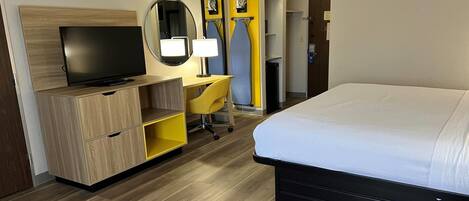 A hotel room with a bed, a TV, a desk with a chair, and a wardrobe.