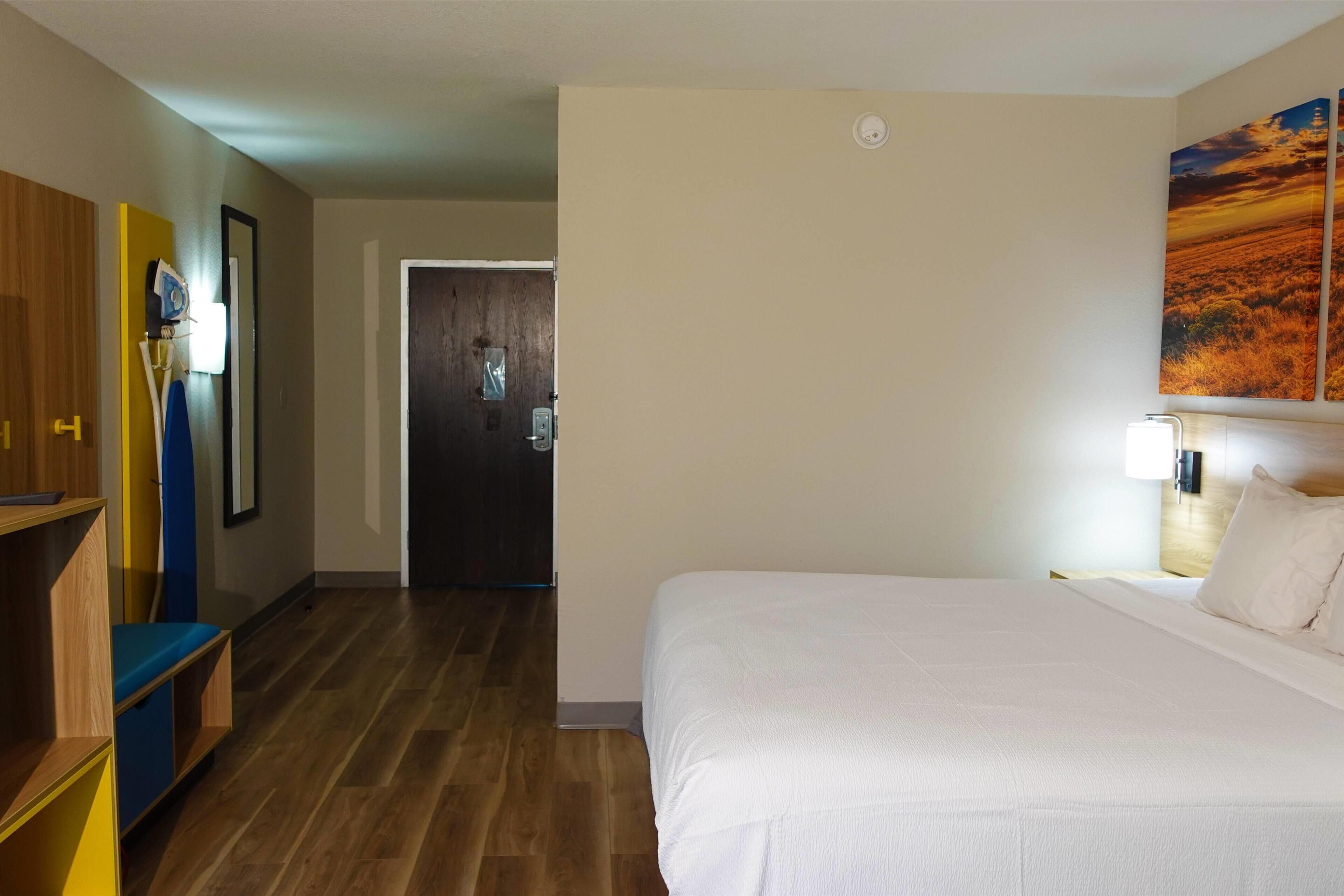 A hotel room with a large bed, a wooden floor, a door leading to another room, and a painting on the wall.