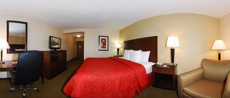 A hotel room with a large bed, a desk with a chair, a small table with a lamp, and a sofa.