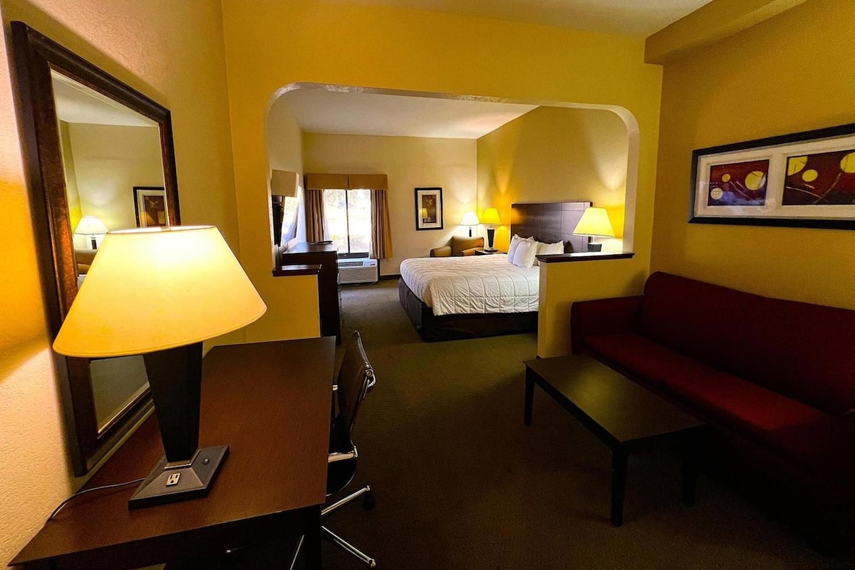 A hotel room with a bed, a desk with a lamp, a red sofa, and a large mirror.