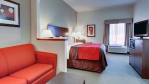 Een hotelkamer met een rode bank, een bed met een rode plaid, een televisie, een bureau en een raam met gordijnen.